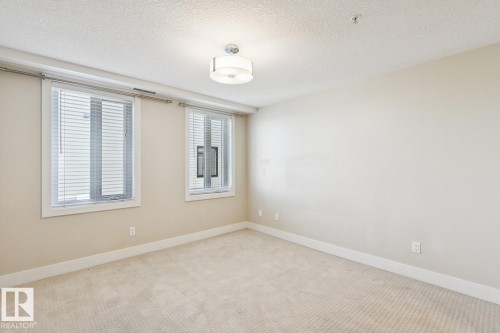 Carpeted spare room with a textured ceiling and baseboards - 208 1350 Windermere Way, Edmonton, AB - Indoor Photo Showing Other Room