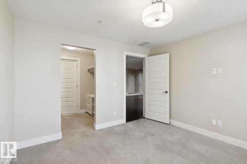 Unfurnished bedroom with light carpet, a walk in closet, and a textured ceiling - 208 1350 Windermere Way, Edmonton, AB - Indoor