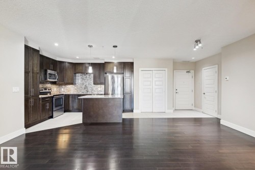 Kitchen featuring dark brown cabinets, stainless steel appliances, decorative light fixtures, recessed lighting, and a center island - 208 1350 Windermere Way, Edmonton, AB - Indoor Photo Showing Kitchen With Stainless Steel Kitchen With Upgraded Kitchen