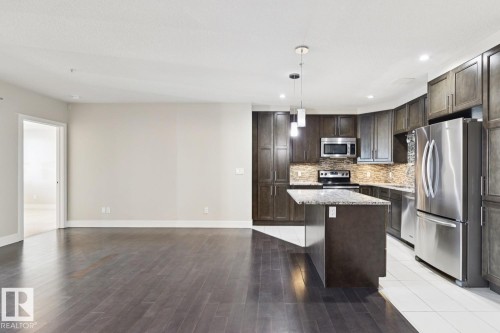 Kitchen with stainless steel appliances, dark brown cabinets, decorative light fixtures, a kitchen island, and recessed lighting - 208 1350 Windermere Way, Edmonton, AB - Indoor Photo Showing Kitchen With Stainless Steel Kitchen With Upgraded Kitchen