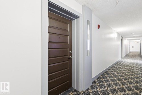 Hallway featuring a textured ceiling and baseboards - 208 1350 Windermere Way, Edmonton, AB - Indoor Photo Showing Other Room