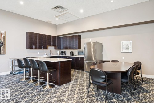 Kitchen featuring a kitchen breakfast bar, dark brown cabinetry, stainless steel appliances, a center island, and light stone countertops - 208 1350 Windermere Way, Edmonton, AB - Indoor