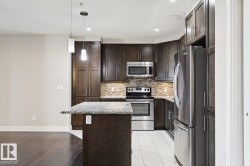 Kitchen with stainless steel appliances, dark brown cabinets, pendant lighting, a center island, and light stone countertops - 