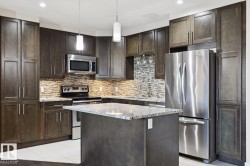 Kitchen with appliances with stainless steel finishes, dark brown cabinetry, light stone counters, pendant lighting, and a kitchen island - 