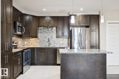 Kitchen with stainless steel appliances, dark brown cabinets, decorative light fixtures, light stone countertops, and recessed lighting - 208 1350 Windermere Way, Edmonton, AB - Indoor Photo Showing Kitchen With Stainless Steel Kitchen With Upgraded Kitchen
