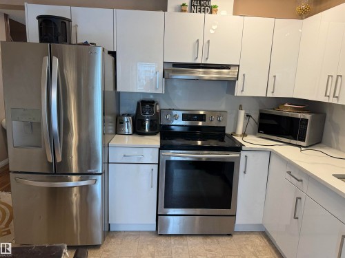 Kitchen with stainless steel appliances, white cabinetry, under cabinet range hood, and light stone counters - 11 15128 22 Street, Edmonton, AB - Indoor Photo Showing Kitchen