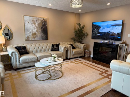 Living room featuring a textured ceiling, wood finished floors, recessed lighting, and a glass covered fireplace - 11 15128 22 Street, Edmonton, AB - Indoor Photo Showing Living Room