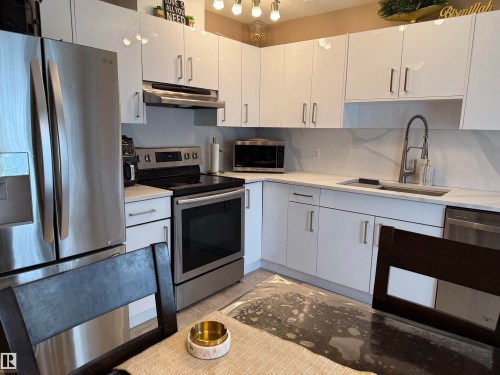 Kitchen with stainless steel appliances, white cabinets, under cabinet range hood, backsplash, and light stone counters - 11 15128 22 Street, Edmonton, AB - Indoor Photo Showing Kitchen With Upgraded Kitchen
