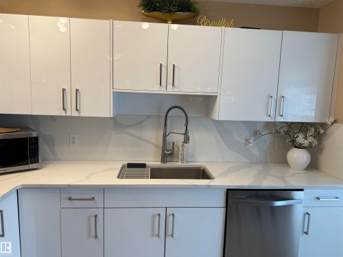 Kitchen featuring white cabinets, stainless steel appliances, backsplash, and light stone counters - 11 15128 22 Street, Edmonton, AB - Indoor Photo Showing Kitchen With Upgraded Kitchen