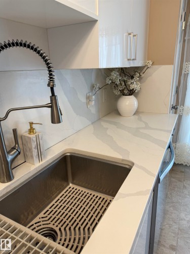 Kitchen view of light stone counters, white cabinets, and tasteful backsplash - 11 15128 22 Street, Edmonton, AB - Indoor Photo Showing Other Room