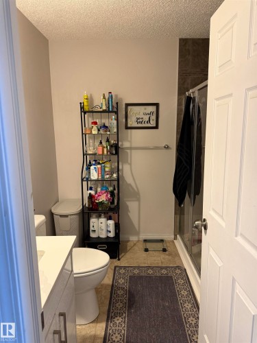 Bathroom with a stall shower, vanity, a textured ceiling, and light tile patterned floors - 11 15128 22 Street, Edmonton, AB - Indoor Photo Showing Bathroom