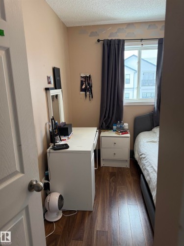 Bedroom with dark wood finished floors, a textured ceiling, and an office area - 11 15128 22 Street, Edmonton, AB - Indoor