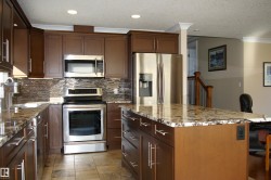 Kitchen with stainless steel appliances, a kitchen island, tasteful backsplash, light stone countertops, and crown molding - 