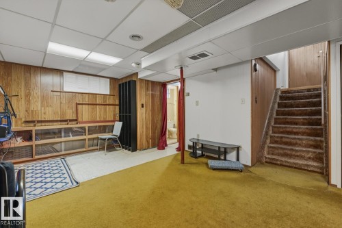 Finished basement featuring a paneled ceiling, wood walls, carpet flooring, and stairs - 11516 152A Avenue, Edmonton, AB - Indoor Photo Showing Basement