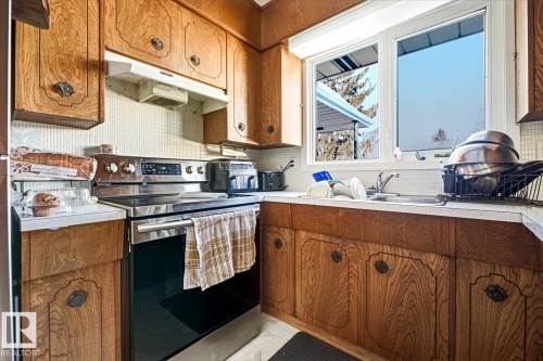 Kitchen with brown cabinetry, stainless steel electric range oven, light countertops, under cabinet range hood, and backsplash - 11516 152A Avenue, Edmonton, AB - Indoor Photo Showing Kitchen