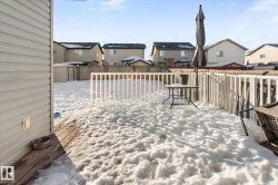 Snow covered patio with a residential view, a fenced backyard, a wooden deck, and a storage unit - 