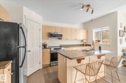 Kitchen featuring stainless steel appliances, a breakfast bar, track lighting, an island with sink, and dark wood-style flooring - 