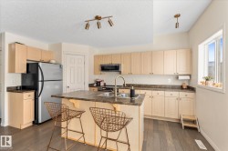 Kitchen featuring stainless steel appliances, a center island with sink, a kitchen bar, dark wood-style flooring, and dark countertops - 