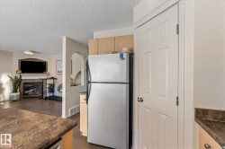Kitchen featuring freestanding refrigerator, light brown cabinetry, open floor plan, dark wood-style floors, and a fireplace - 
