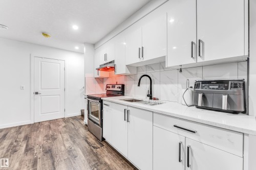 Kitchen with electric stove, white cabinets, dark wood-style flooring, light stone countertops, and tasteful backsplash - 2095 Maple Road, Edmonton, AB - Indoor Photo Showing Kitchen