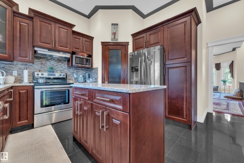 Kitchen featuring stainless steel appliances, granite tiled floors, light stone counters, ornamental molding, and under cabinet range hood - 2012 69 Street, Edmonton, AB - Indoor Photo Showing Kitchen