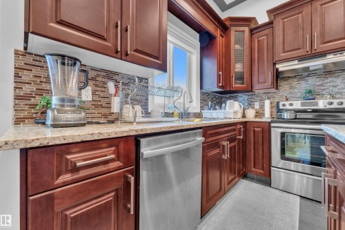 Kitchen with stainless steel appliances, light stone countertops, under cabinet range hood, light tile patterned floors, and decorative backsplash - 2012 69 Street, Edmonton, AB - Indoor Photo Showing Kitchen