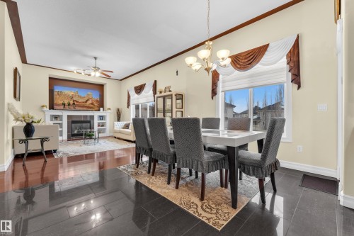 Dining area with granite tiled floors, ceiling fan, a tiled fireplace, a chandelier, and crown molding - 2012 69 Street, Edmonton, AB - Indoor Photo Showing Dining Room With Fireplace