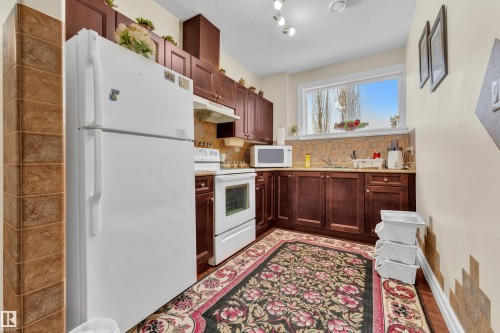 Kitchen featuring white appliances, under cabinet range hood, a textured ceiling, backsplash, and dark wood-style floors - 2012 69 Street, Edmonton, AB - Indoor Photo Showing Kitchen