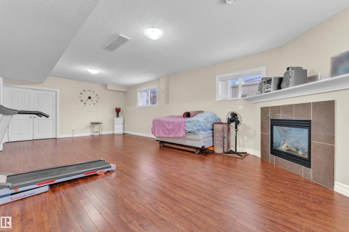 Workout area with hardwood / wood-style floors, a tiled fireplace, and a textured ceiling - 2012 69 Street, Edmonton, AB - Indoor Photo Showing Living Room With Fireplace