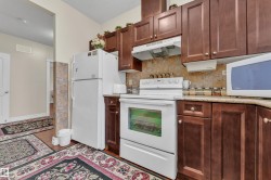 Kitchen featuring white appliances, under cabinet range hood, dark wood-style floors, a textured ceiling, and decorative backsplash - 