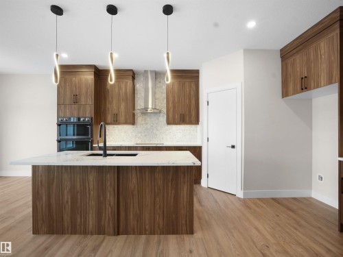 Kitchen with modern cabinets, light stone counters, decorative backsplash, a center island with sink, and hanging light fixtures - 46 Waverly Way, Fort Saskatchewan, AB - Indoor Photo Showing Kitchen
