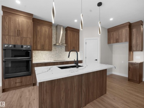 Kitchen with light stone counters, modern cabinets, light wood finished floors, decorative backsplash, and wall chimney range hood - 46 Waverly Way, Fort Saskatchewan, AB - Indoor Photo Showing Kitchen With Double Sink