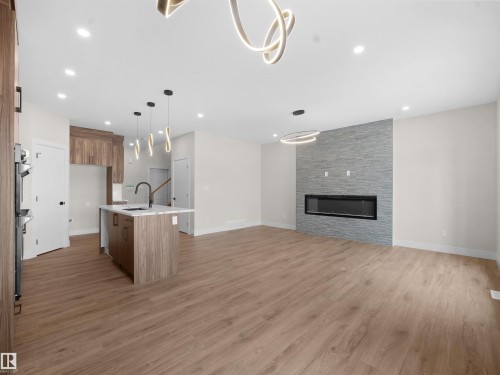 Kitchen with an island with sink, open floor plan, decorative light fixtures, light wood-style flooring, and a fireplace - 46 Waverly Way, Fort Saskatchewan, AB - Indoor With Fireplace