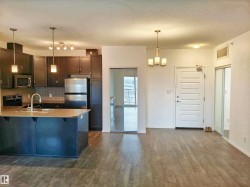 Kitchen featuring light countertops, a textured ceiling, appliances with stainless steel finishes, hanging light fixtures, and a chandelier - 