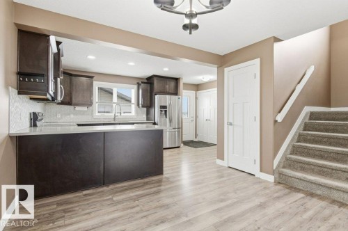 Kitchen with dark brown cabinetry, stainless steel refrigerator with ice dispenser, light wood-style flooring, a peninsula, and stove - 2 Wingate Way, Fort Saskatchewan, AB - Indoor Photo Showing Kitchen