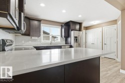 Kitchen featuring dark brown cabinets, appliances with stainless steel finishes, light stone countertops, a peninsula, and light wood-type flooring - 