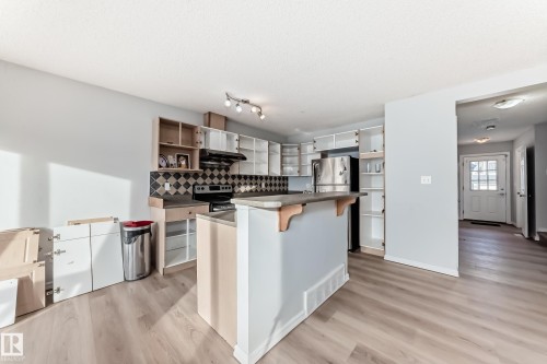 Kitchen with a breakfast bar, open shelves, light wood-style flooring, backsplash, and a textured ceiling - 7731 8 Avenue, Edmonton, AB - Indoor Photo Showing Kitchen