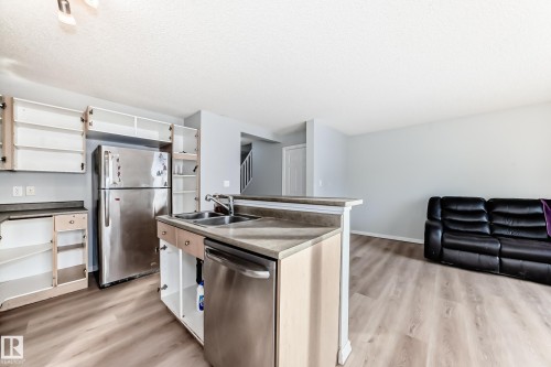 Kitchen featuring stainless steel appliances, open shelves, light wood-type flooring, open floor plan, and a kitchen island with sink - 7731 8 Avenue, Edmonton, AB - Indoor Photo Showing Kitchen With Stainless Steel Kitchen With Double Sink