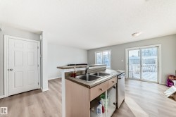 Kitchen featuring an island with sink, light wood-style floors, light brown cabinetry, dishwasher, and dark countertops - 
