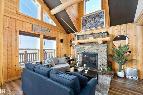 Living area featuring wooden walls, high vaulted ceiling, a stone fireplace, dark wood-type flooring, and beam ceiling - 19003 Twp Rd 522, Rural Beaver County, AB - Indoor Photo Showing Living Room With Fireplace
