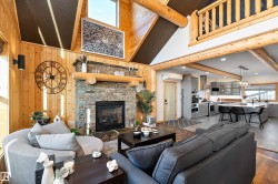 Living room with a stone fireplace, wooden walls, wood finished floors, high vaulted ceiling, and recessed lighting - 