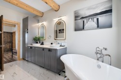 Full bathroom featuring double vanity, beamed ceiling, light marble finish floors, and a freestanding bath - 