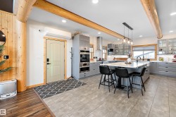 Kitchen featuring gray cabinets, decorative light fixtures, a kitchen bar, beam ceiling, and an island with sink - 