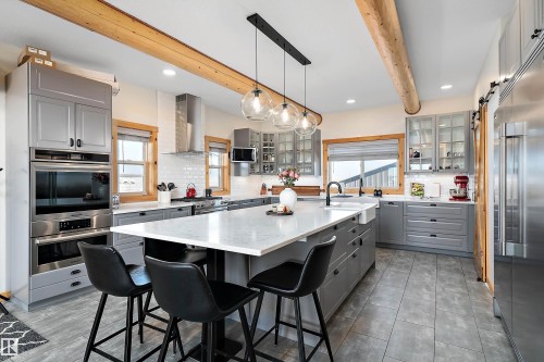 Kitchen with gray cabinets, decorative light fixtures, a barn door, beam ceiling, and tasteful backsplash - 19003 Twp Rd 522, Rural Beaver County, AB - Indoor Photo Showing Kitchen With Upgraded Kitchen