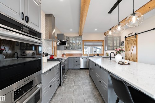 Kitchen with a barn door, decorative light fixtures, beam ceiling, appliances with stainless steel finishes, and light stone counters - 19003 Twp Rd 522, Rural Beaver County, AB - Indoor Photo Showing Kitchen With Upgraded Kitchen