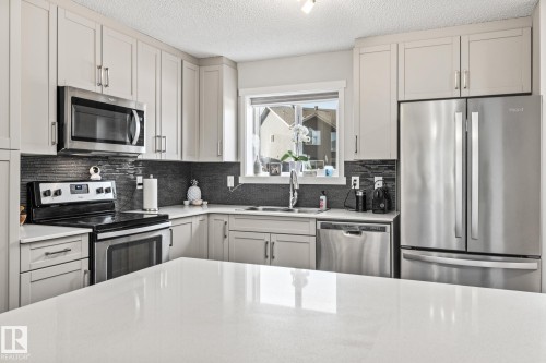 Kitchen featuring stainless steel appliances, light stone counters, a textured ceiling, and backsplash - 20110 27 Avenue, Edmonton, AB - Indoor Photo Showing Kitchen With Double Sink With Upgraded Kitchen