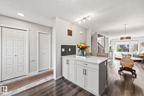 Kitchen featuring a peninsula, a textured ceiling, dark wood-style floors, light stone countertops, and white cabinets - 20110 27 Avenue, Edmonton, AB - Indoor