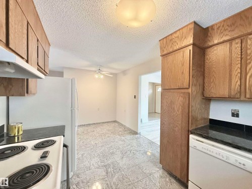 Kitchen featuring white appliances, a textured ceiling, a ceiling fan, brown cabinetry, and dark stone counters - 2112 104B Street, Edmonton, AB - Indoor Photo Showing Kitchen