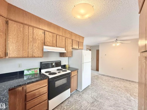 Kitchen with white appliances, under cabinet range hood, a textured ceiling, ceiling fan, and dark stone countertops - 2112 104B Street, Edmonton, AB - Indoor Photo Showing Kitchen