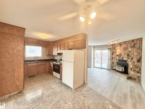 Kitchen featuring white appliances, dark countertops, a textured ceiling, a wood stove, and brown cabinetry - 2112 104B Street, Edmonton, AB - Indoor Photo Showing Kitchen With Fireplace
